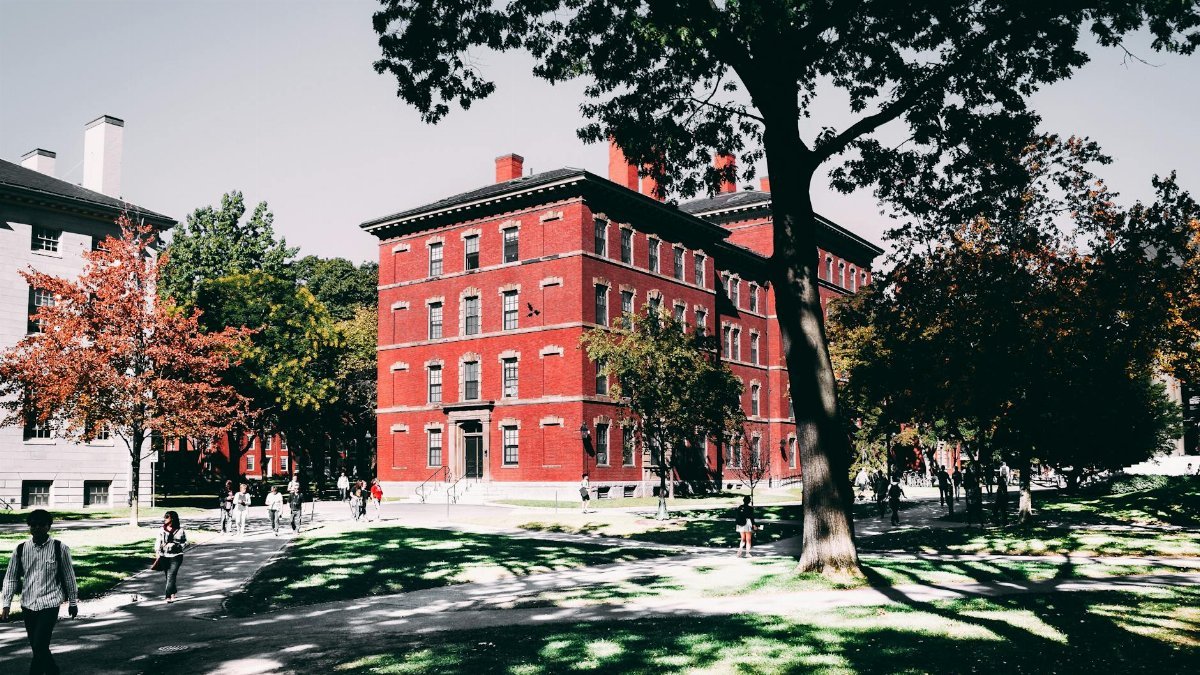 View of a historic red brick university building surrounded by lush trees and walking paths.