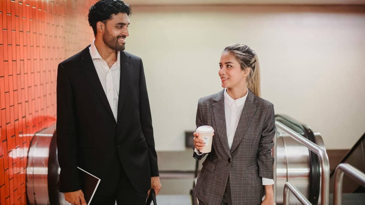 Two business professionals conversing indoors, dressed in formal attire with coffee and accessories.