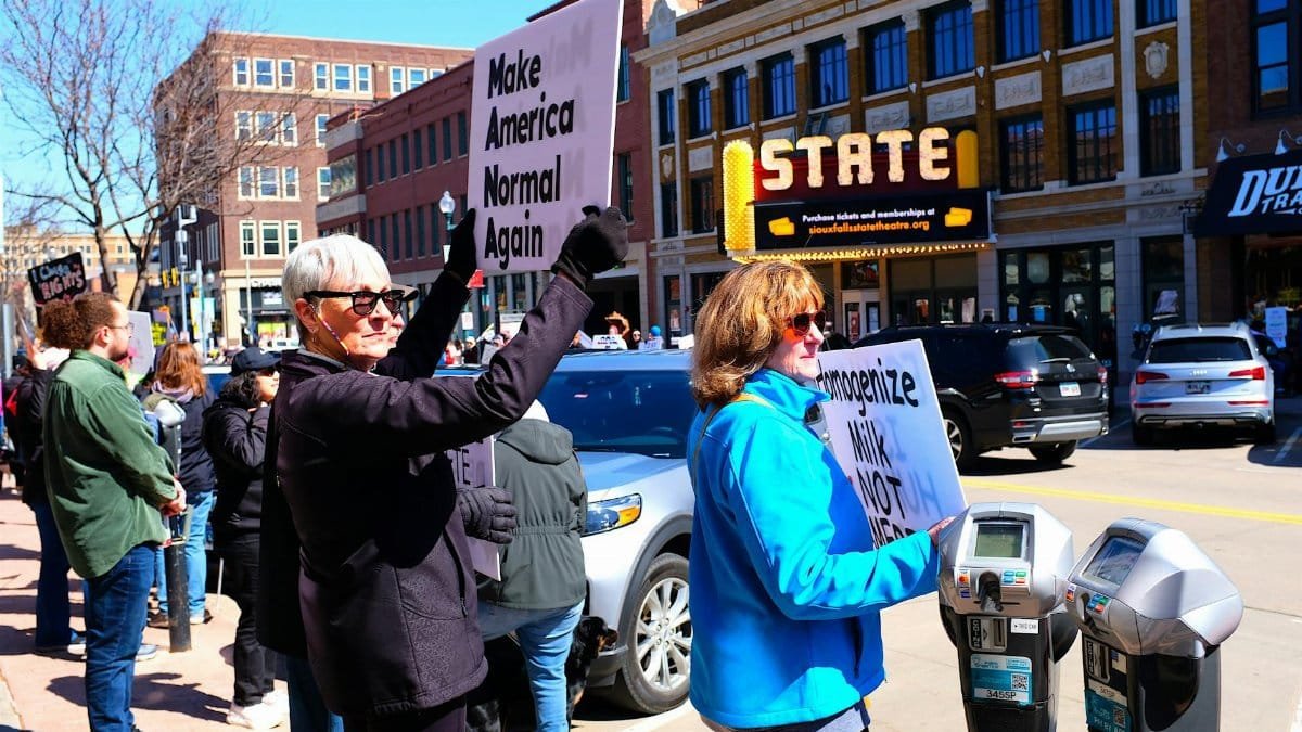 People protesting outside a small town theater with signs about social issues.