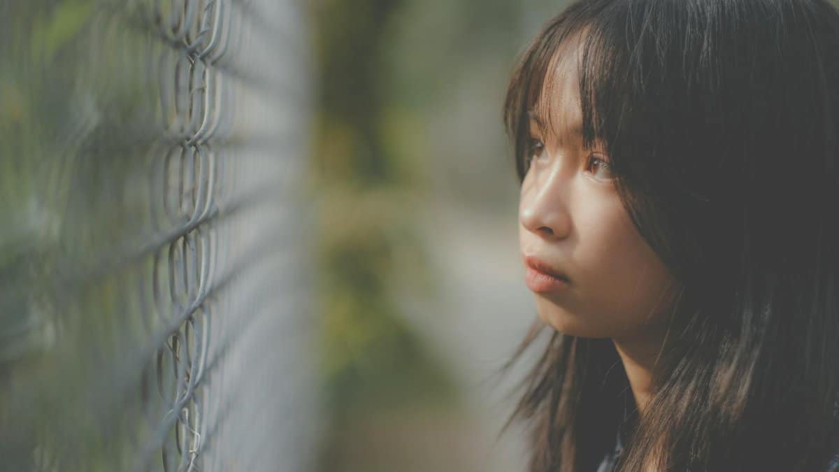Side view of serious ethnic girl with long dark hair and brown eyes looking through metal fence
