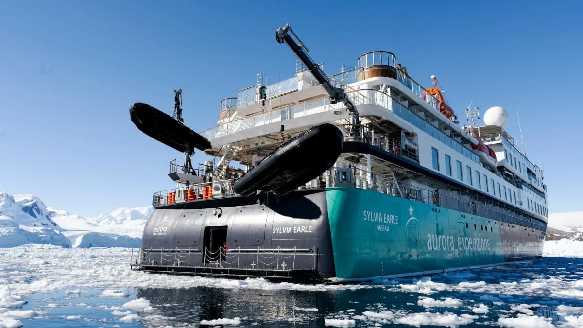 The expedition ship Sylvia Earle navigating icy waters in the Arctic, surrounded by stunning icebergs and clear skies.