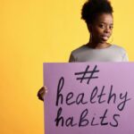 Portrait of a woman holding a healthy habits sign, set against a vibrant yellow background.