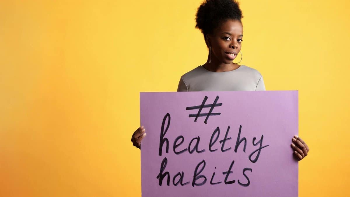 Portrait of a woman holding a healthy habits sign, set against a vibrant yellow background.