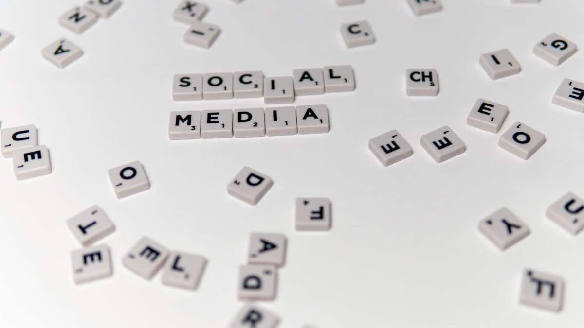 White Scrabble tiles forming the phrase 'social media' on a scattered background.