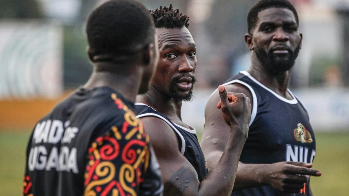Three male athletes discussing strategy during a sports event in Uganda.