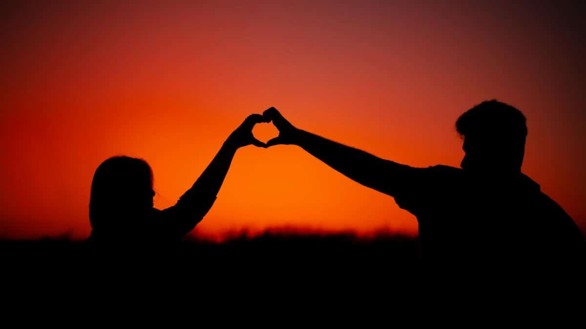Silhouette of a couple forming a heart shape with hands during a romantic sunset.