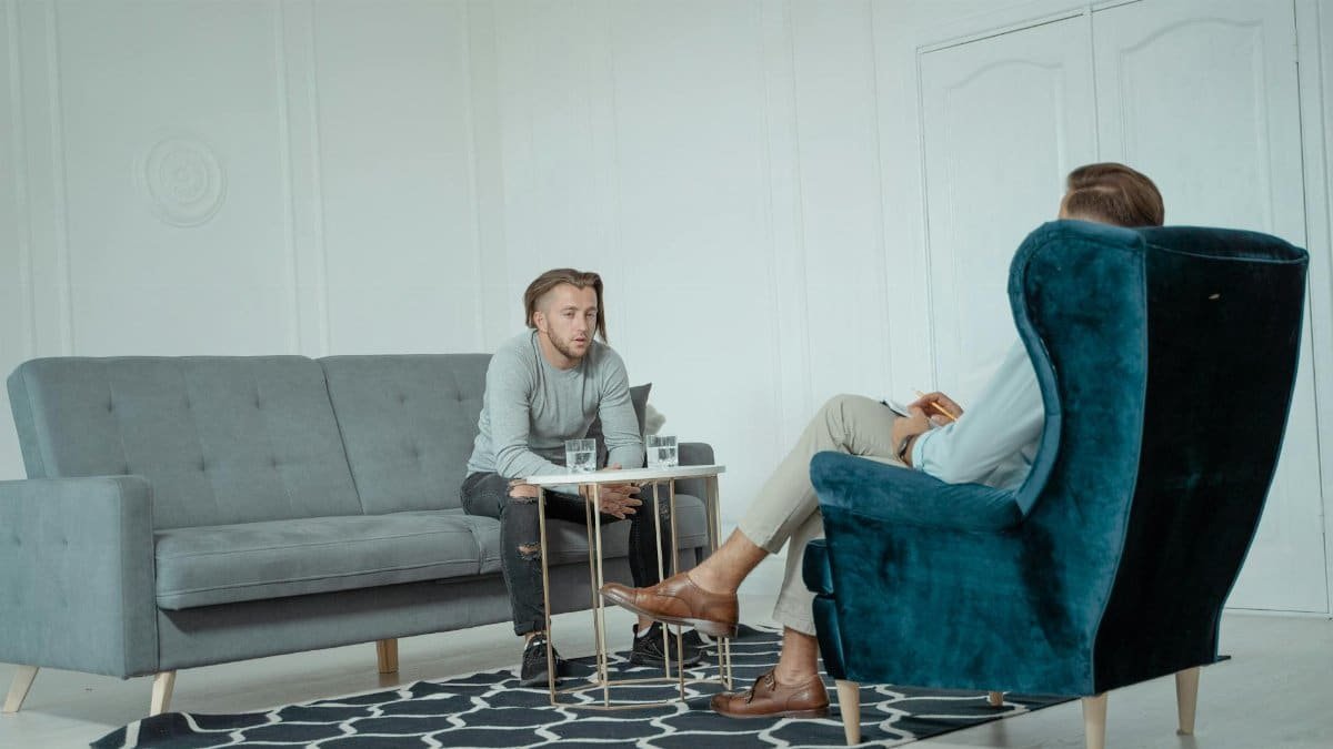 Two men engaged in a therapy session inside a modern office setting, discussing mental health.