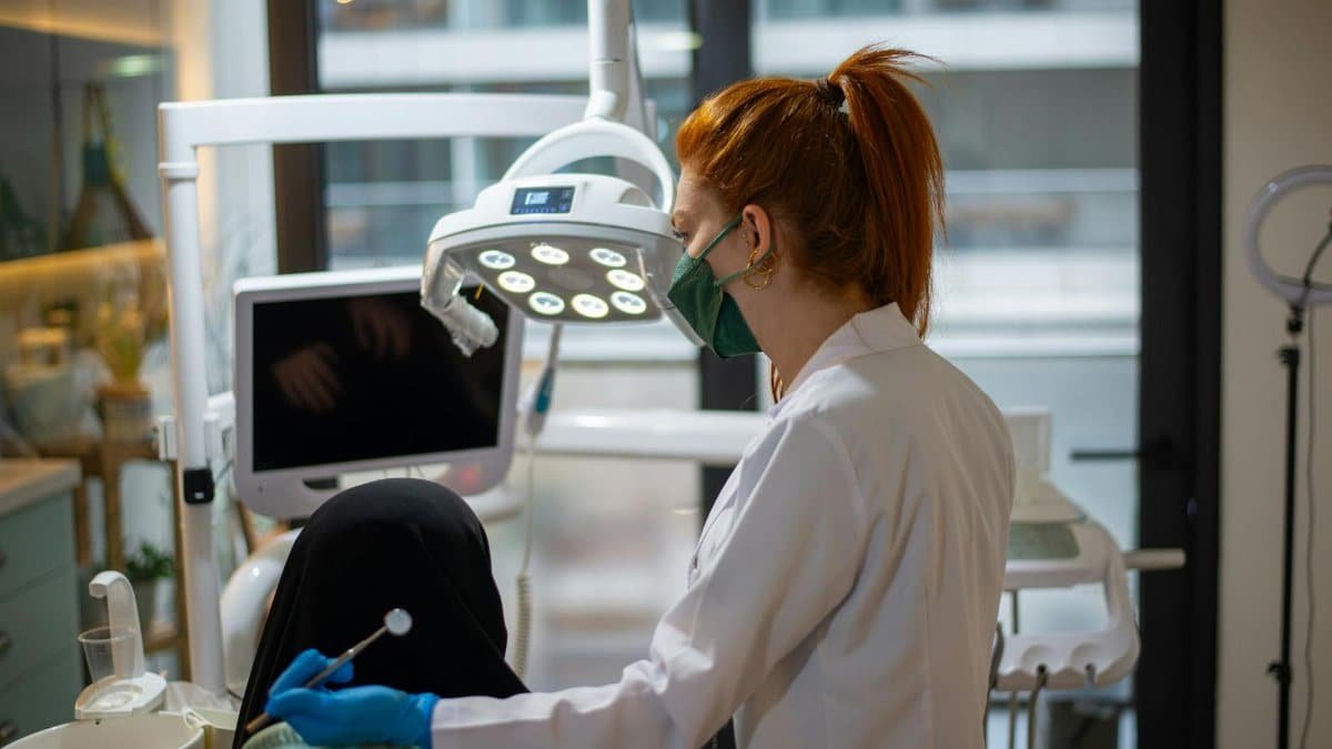 A dentist wearing a mask attends to a patient in a modern dental clinic with advanced equipment.