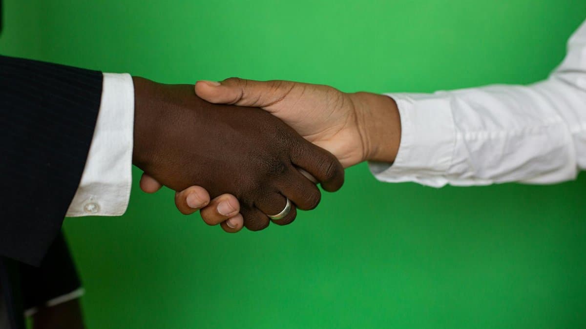 Two diverse hands shaking towards a successful business deal on a green background.