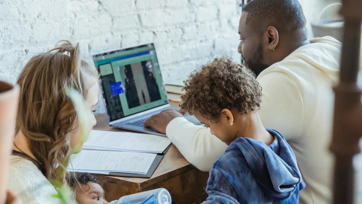High angle of African American dad watching laptop working near son playing toys and mother feeding little infant