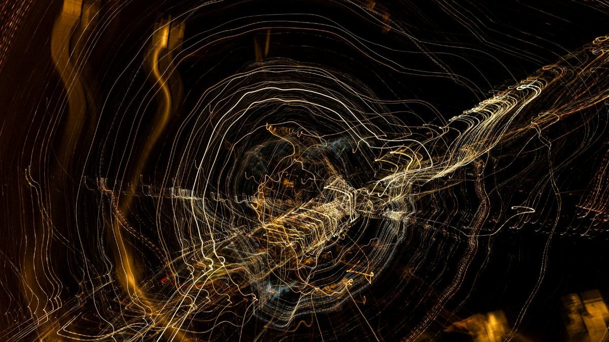 Swirling light trails create an abstract pattern against a dark background, evoking motion and energy.