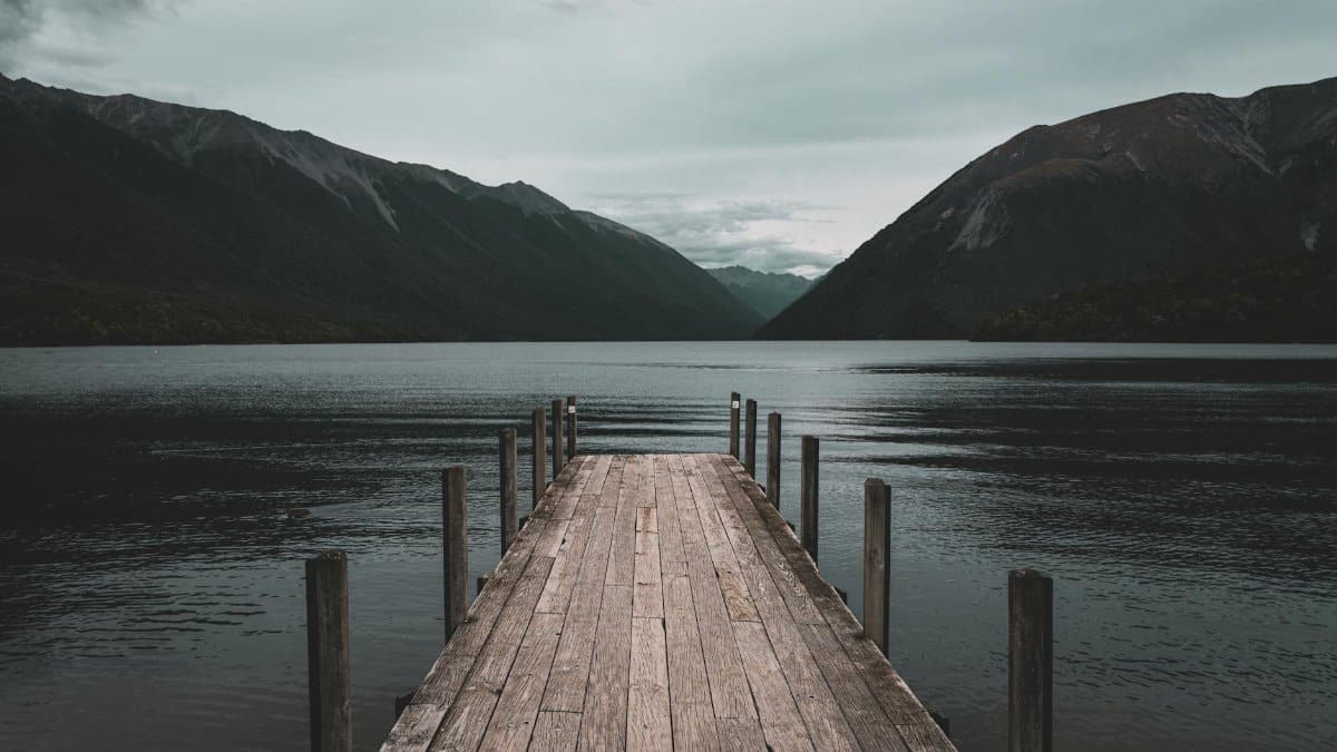 A wooden pier leading out onto a peaceful lake with mountainous backdrop, perfect for tranquil travel and nature-themed projects.