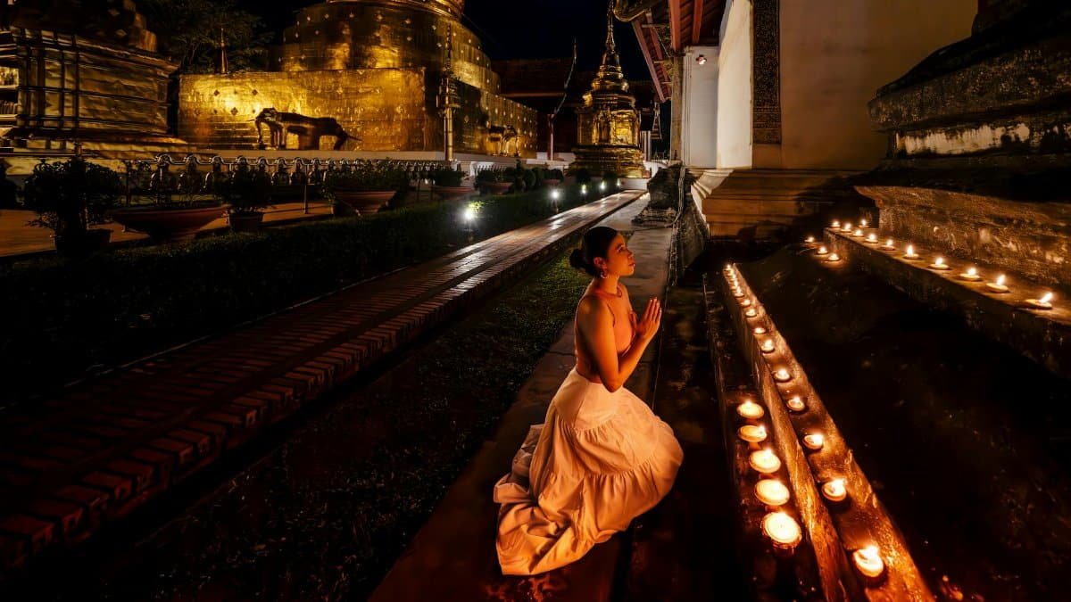 A woman prays surrounded by candles in a temple at night, creating a serene and spiritual atmosphere.