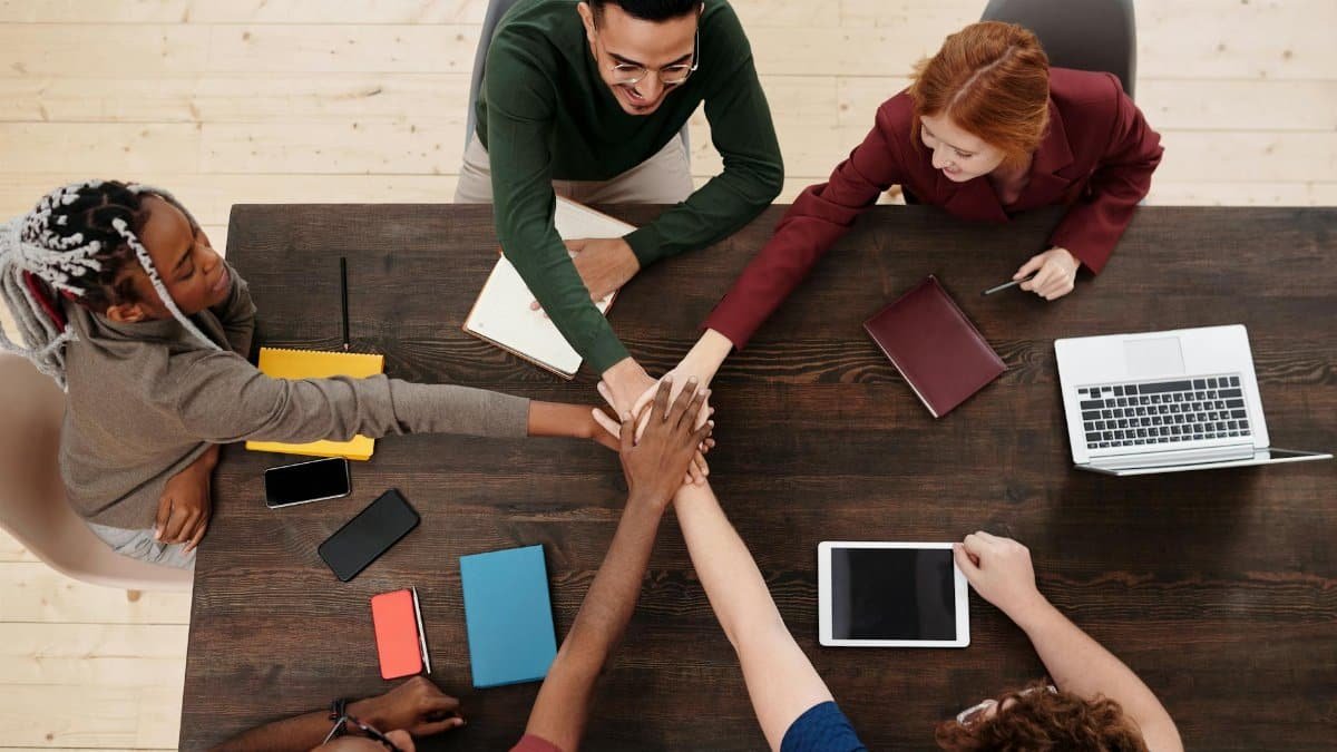 Top view of a diverse team stacking hands in unity over a wooden table, displaying teamwork.