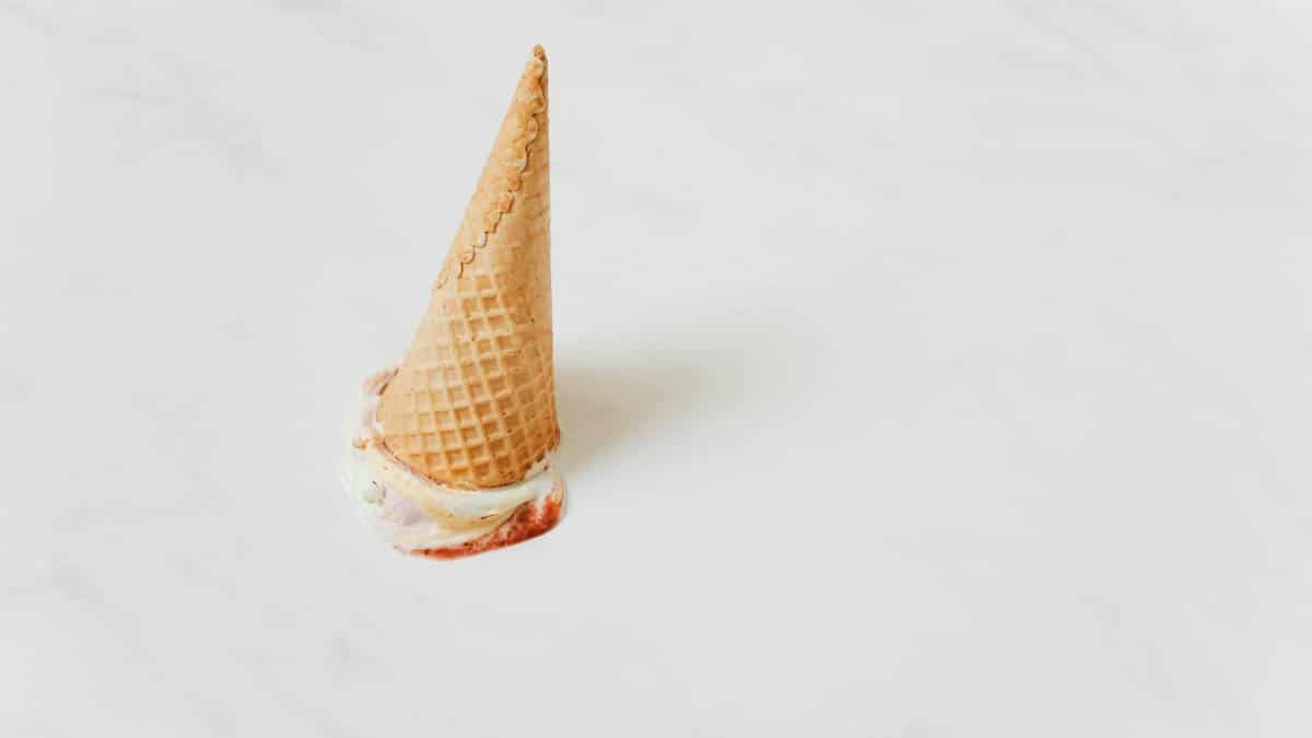 An upside-down ice cream cone melting on a white marble surface.
