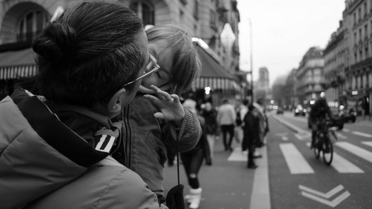 A candid father and child moment captured on a busy city street in black and white.