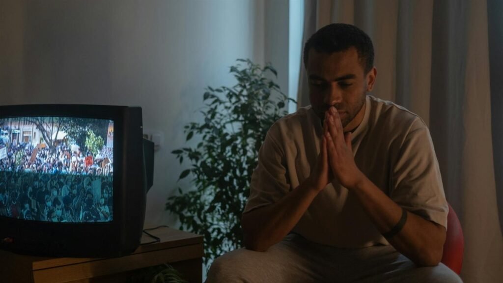 A man seated indoors in reflection during quarantine, TV on.