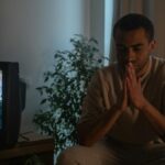 A man seated indoors in reflection during quarantine, TV on.