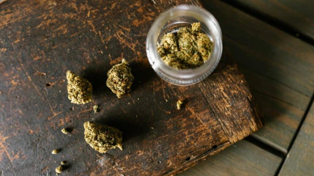 Cannabis buds scattered on a rustic wooden surface with an open jar.