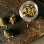 Cannabis buds scattered on a rustic wooden surface with an open jar.