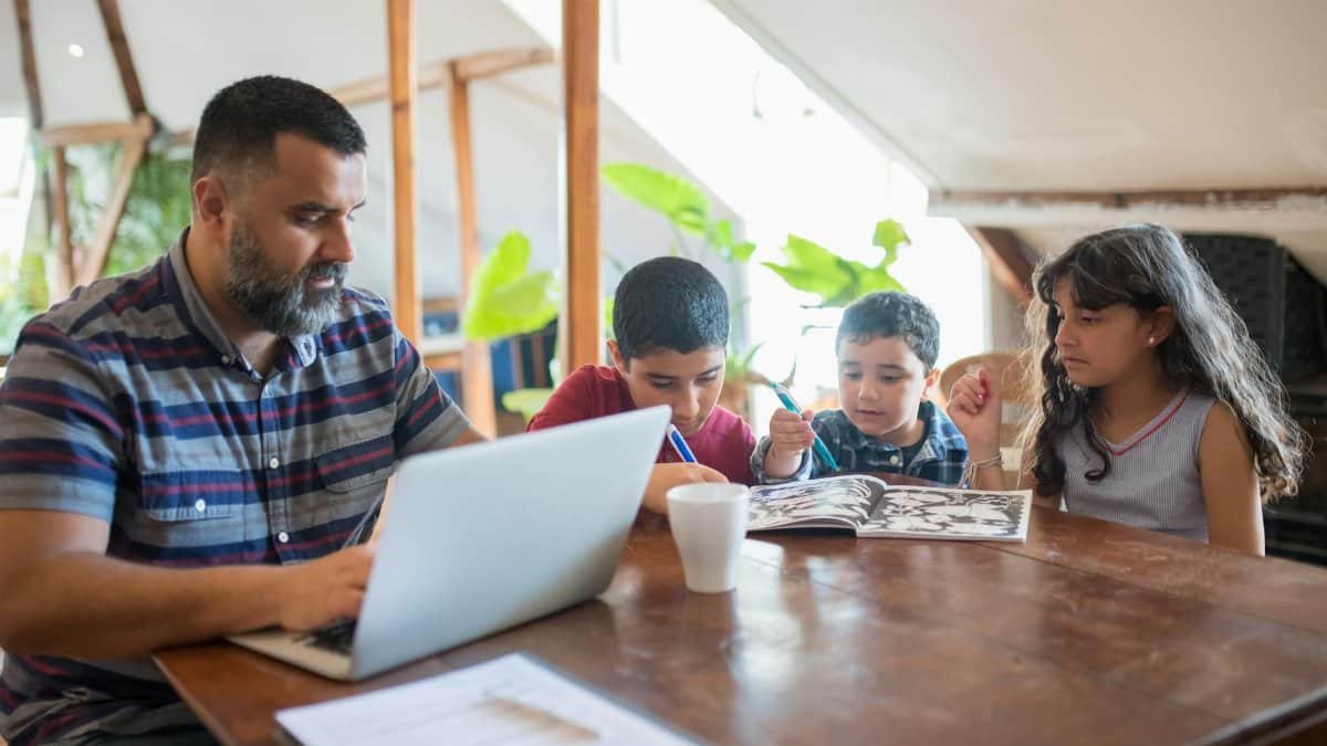 A father multitasks with a laptop and children at home, illustrating work-life balance.