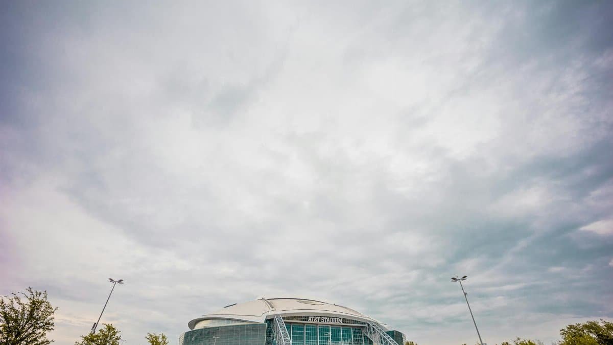 Wide-angle view of AT&T Stadium under dramatic clouds highlighting modern architectural design.