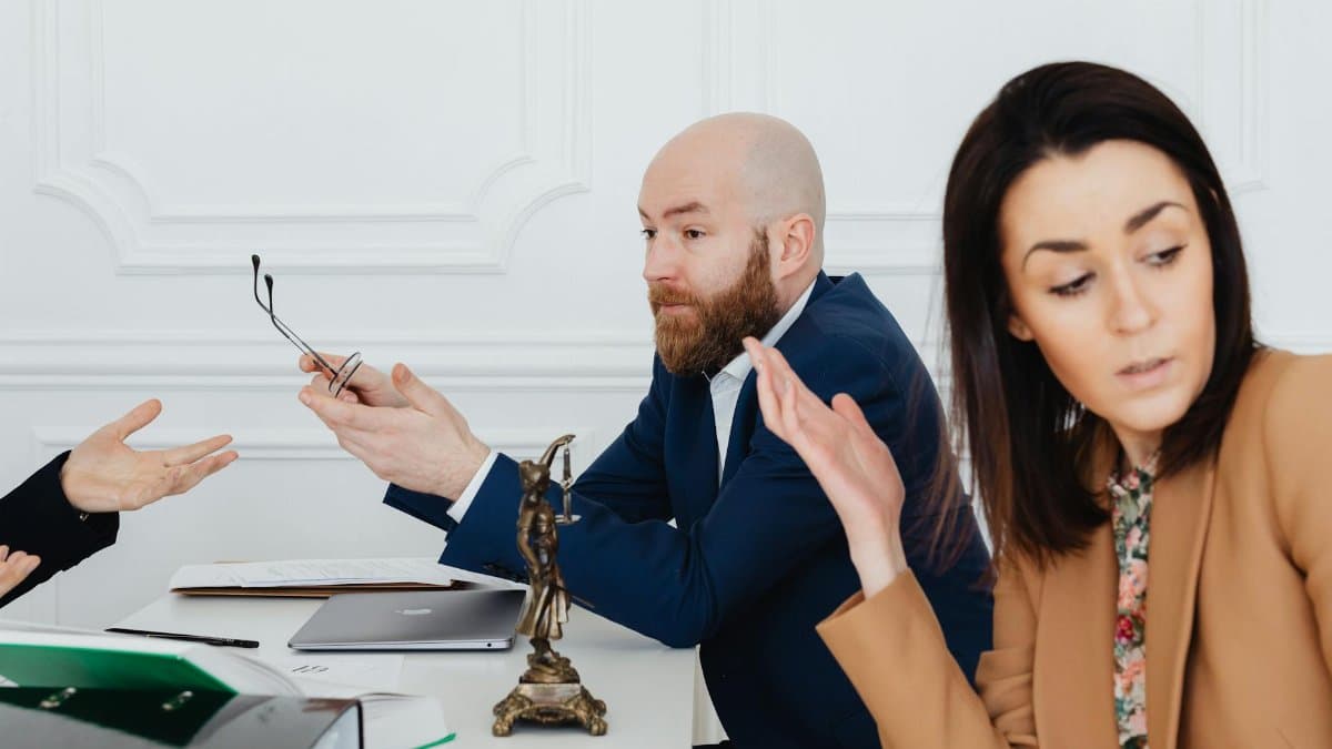 Three adults in a heated discussion with legal documents, indoors.
