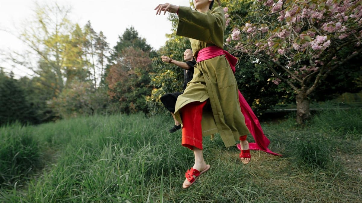 Two people dancing joyfully in traditional wear surrounded by cherry blossoms in a serene Japanese garden.