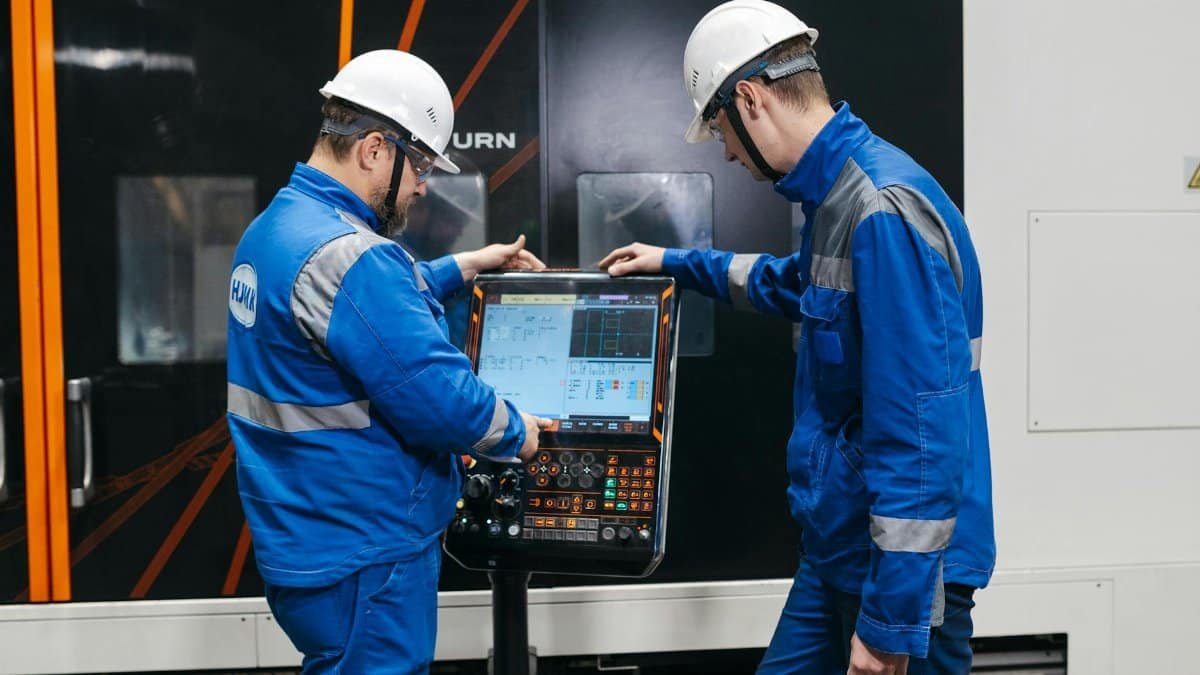 Two engineers operating CNC machinery in a factory setting, wearing safety gear and uniforms.