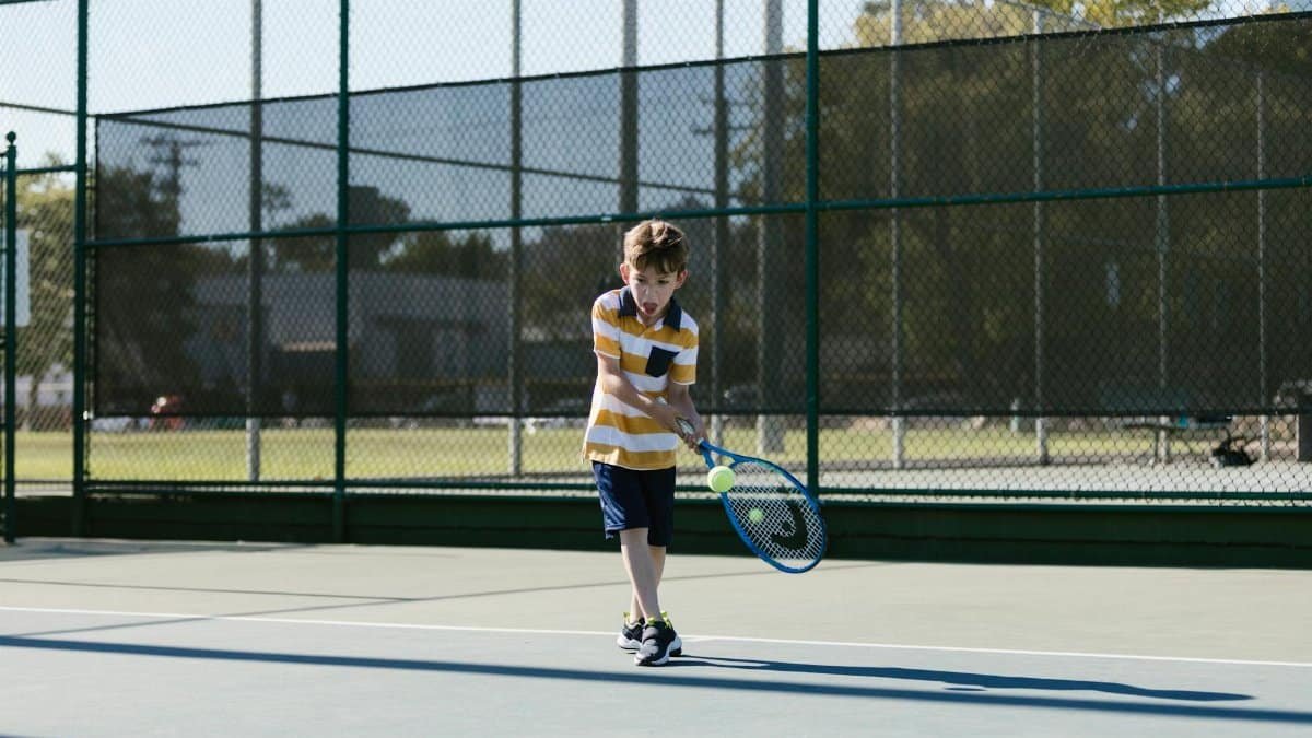 A young boy practicing tennis on an outdoor court, focusing on hitting backhand shots.