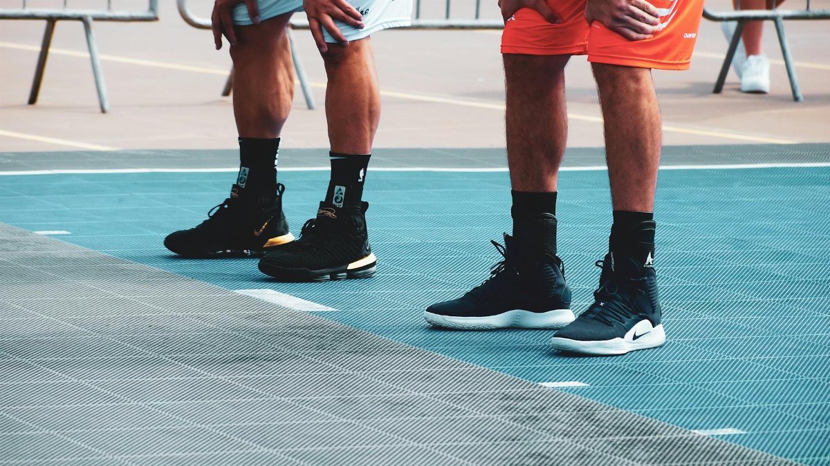Athletes standing on basketball court, ready for game, focusing on footwear and posture.