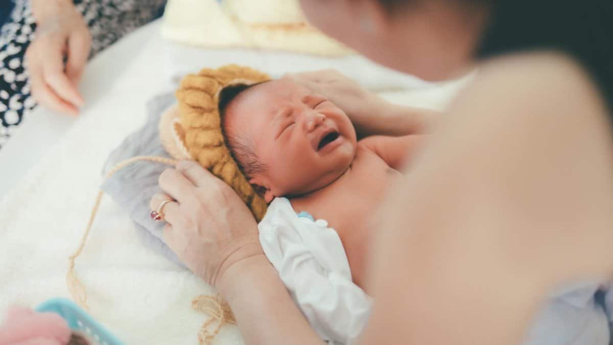 A crying newborn baby lying on a bed while being comforted by a parent, showcasing early life moments.