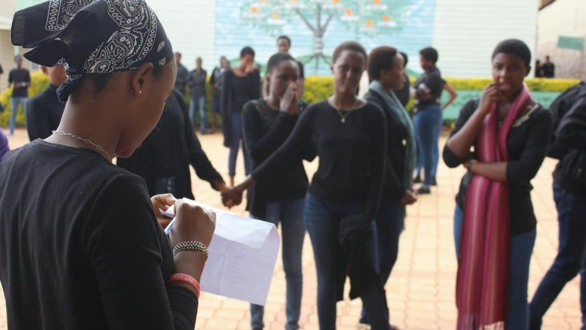 Women gathered outdoors in Burundi, engaging in community activities and reading a paper.