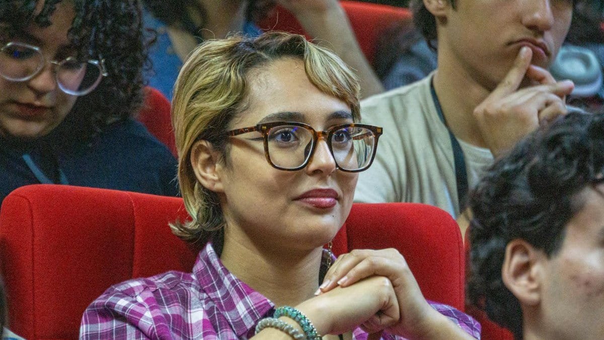 Young adults attentively listening during a conference session, seated in a lecture hall.