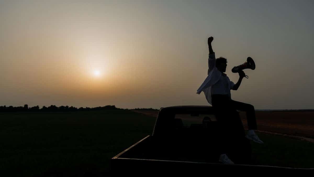 Silhouette of a person with a megaphone on a truck at sunset, symbolizing activism.