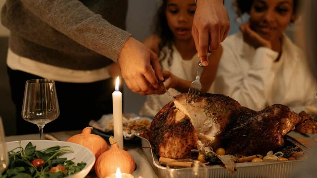 Family carving a Thanksgiving turkey at a festive dinner table indoors, warm candlelight.