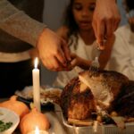 Family carving a Thanksgiving turkey at a festive dinner table indoors, warm candlelight.