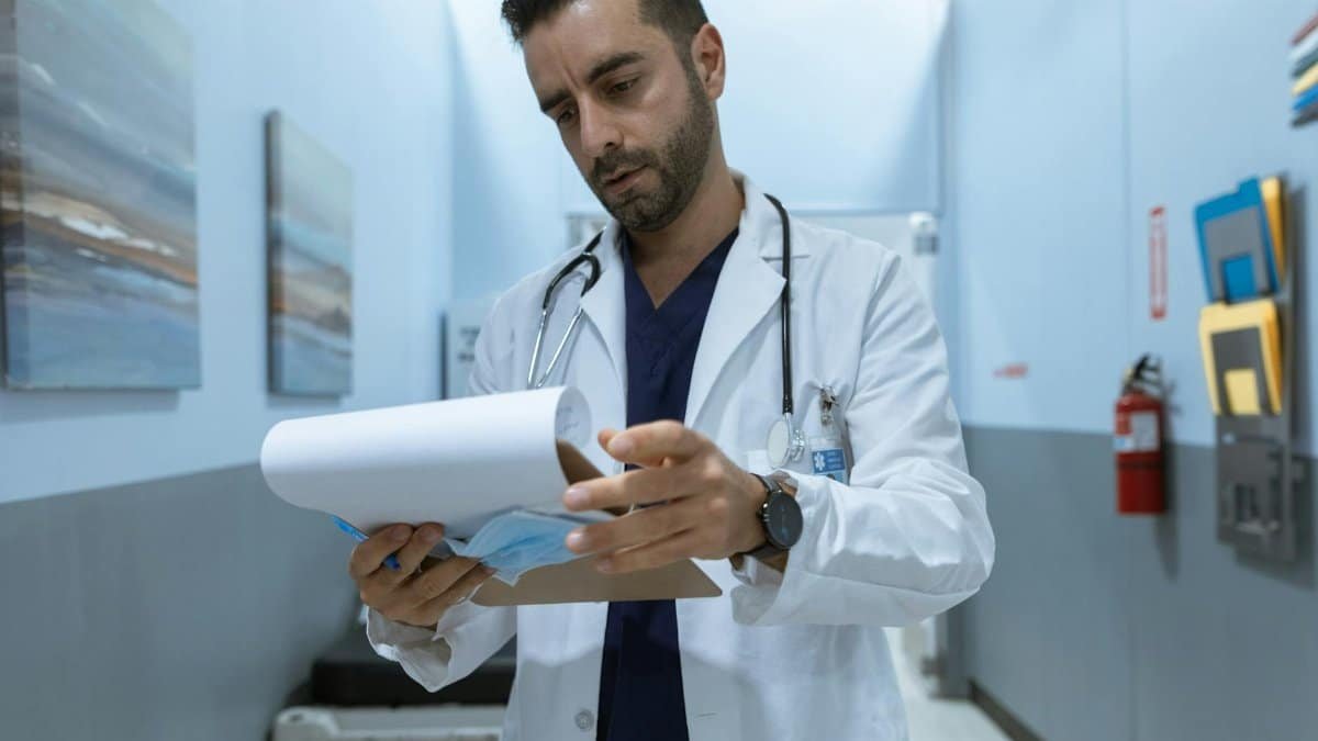 Male doctor in hospital hallway reviewing medical charts, focused and dedicated.