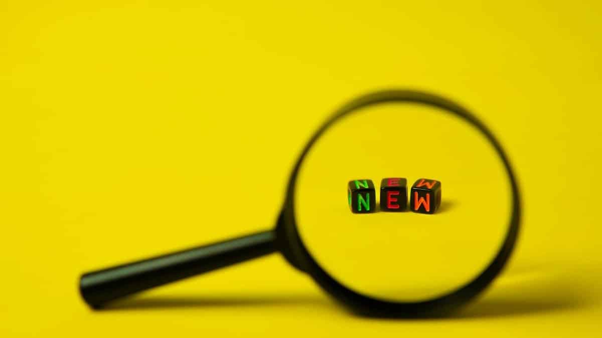 Concept image of big black magnifier with word new in form of cubes against yellow background