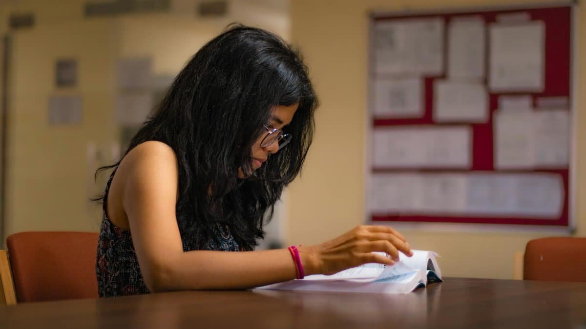 Focused young woman reading a textbook at a university library desk in New Delhi.