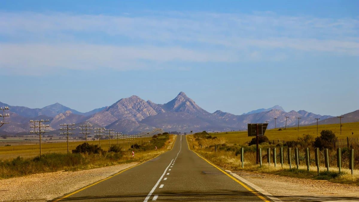 Wide open road leading to stunning mountain range under clear blue sky.