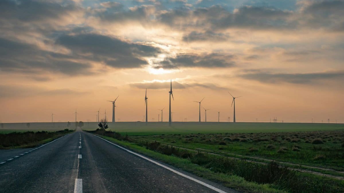 A picturesque rural road leading to wind turbines under a vibrant sunset in Romania, emphasizing renewable energy.
