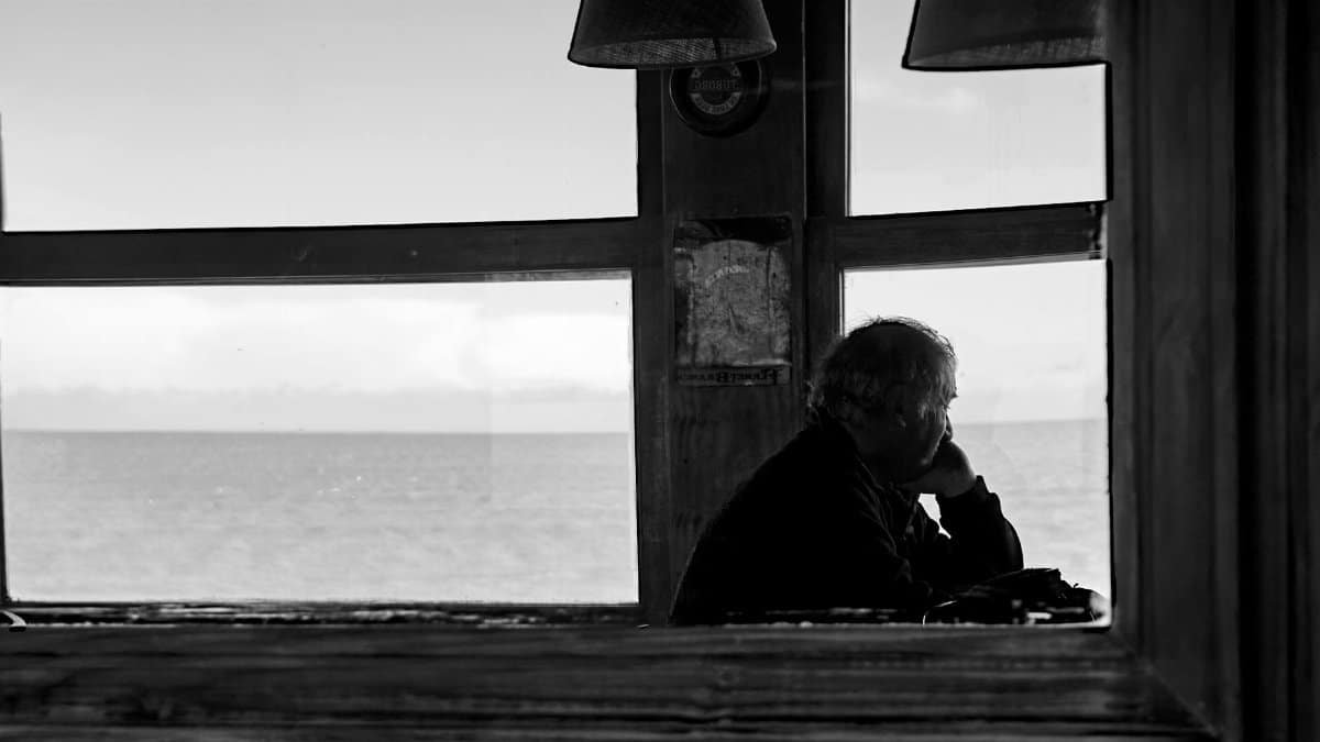 Silhouette of a man looking out a window at the sea in a monochrome view, reflecting solitude.