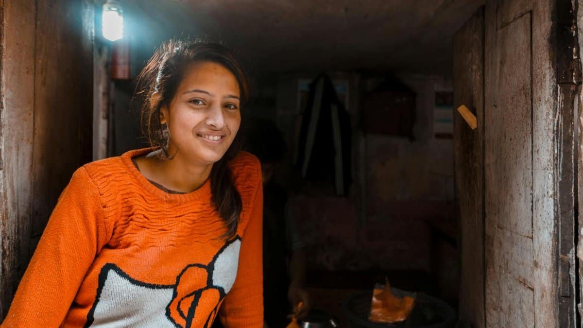 A young woman smiling warmly in a cozy orange knitted sweater, indoors.