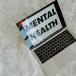 A laptop on a fluffy surface highlights the phrase 'Mental Health', emphasizing awareness.