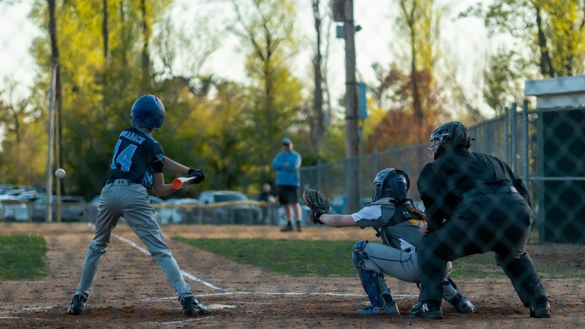 Exciting youth baseball game featuring a batter, catcher, and umpire in action at dusk.