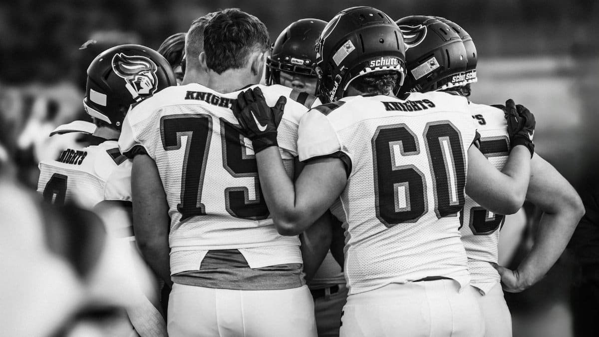 High school football team players huddle in a moment of unity before the game, emphasizing teamwork and strategy.