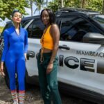 Two stylish women stand beside a Miami Beach police car in a sunny outdoor setting.