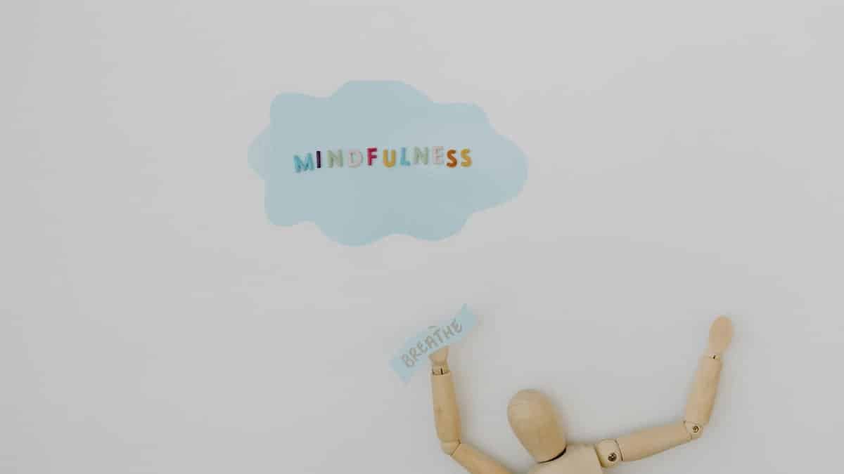 Wooden figure holding 'breathe' text with 'mindfulness' cloud on white background.