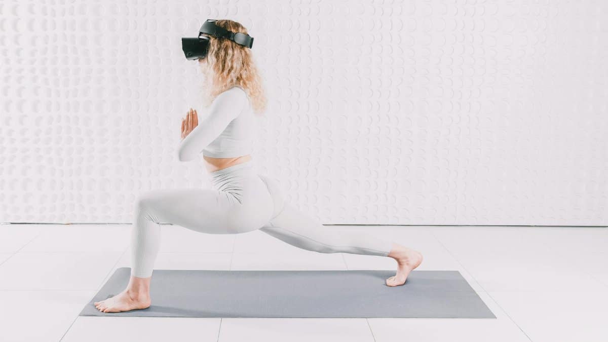 Adult woman in yoga pose wearing VR headset, exploring virtual reality indoors on a mat.
